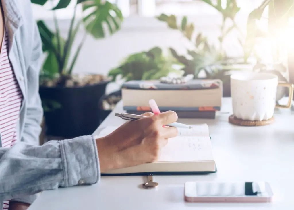 daily intentions: mom writing in journal on a peaceful table with coffee and books and plants