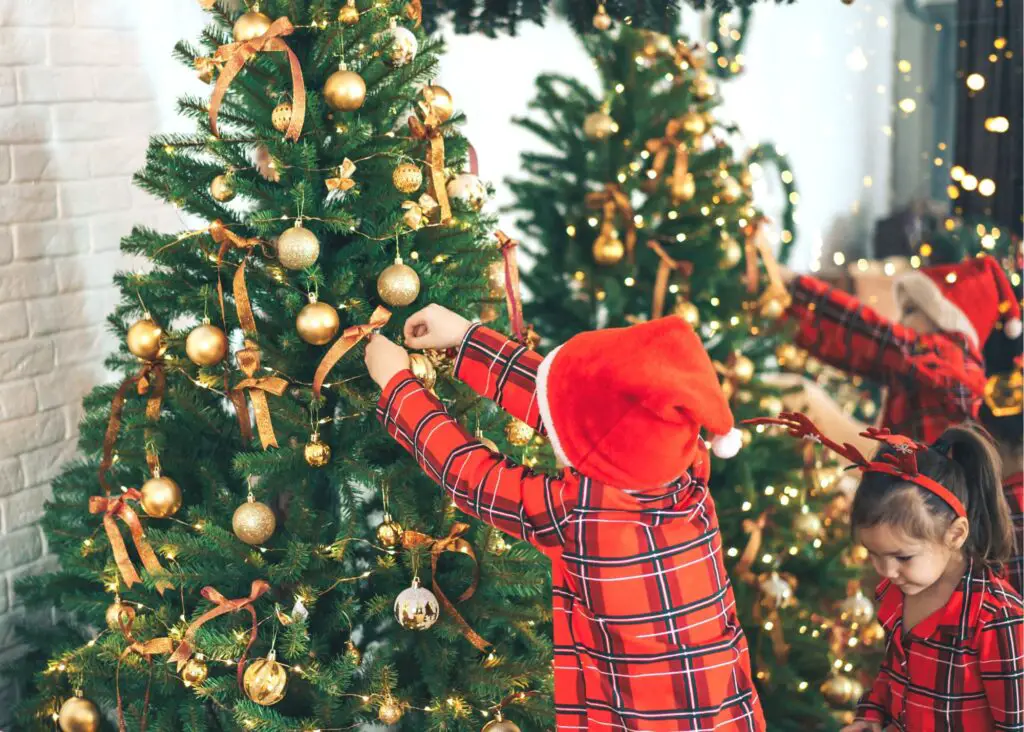 Family Matching Christmas Pajamas: 2 kids decorating the tree in matching plaid red christmas pajamas and santa hats.