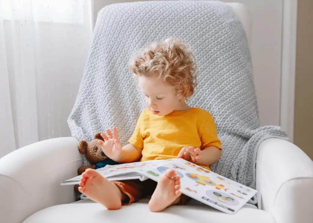 toddler boy with blonde curls sitting in a comfy chair reading a book: trendy middle names for jack