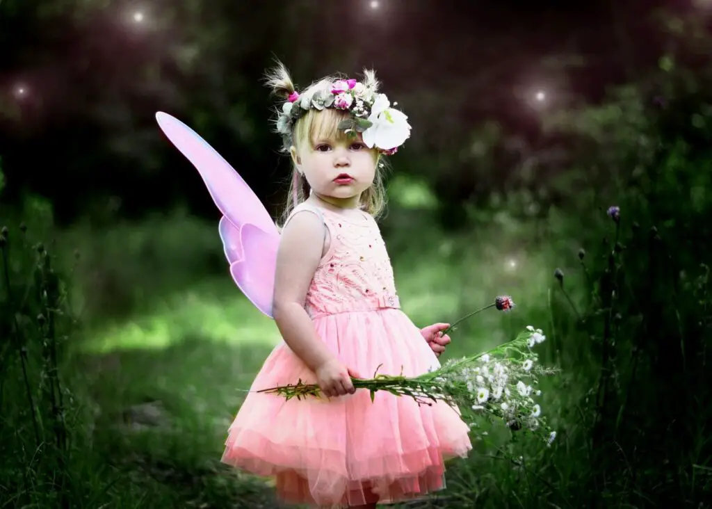 ethereal girl names: toddler girl in pink tutu dress with pink fairy wings, flower crown and wildflower bouquet in a mystical, natural setting