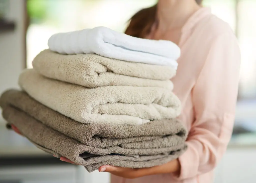 daily cleaning habits: one load of laundry a day. Mom holding stack of brown and beige towels